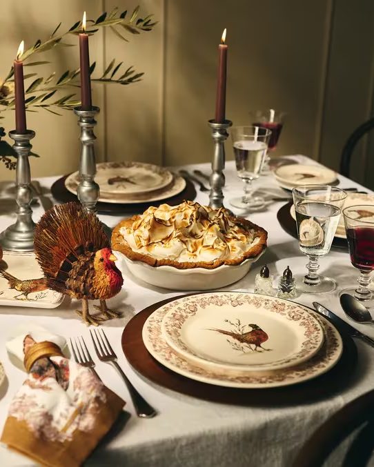 A holiday table set with Sur La Table dinnerware, candles and a pie